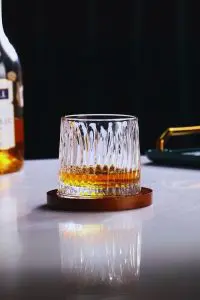 Verre à whisky tumbler rempli, posé sur son socle en bois sur une table claire.