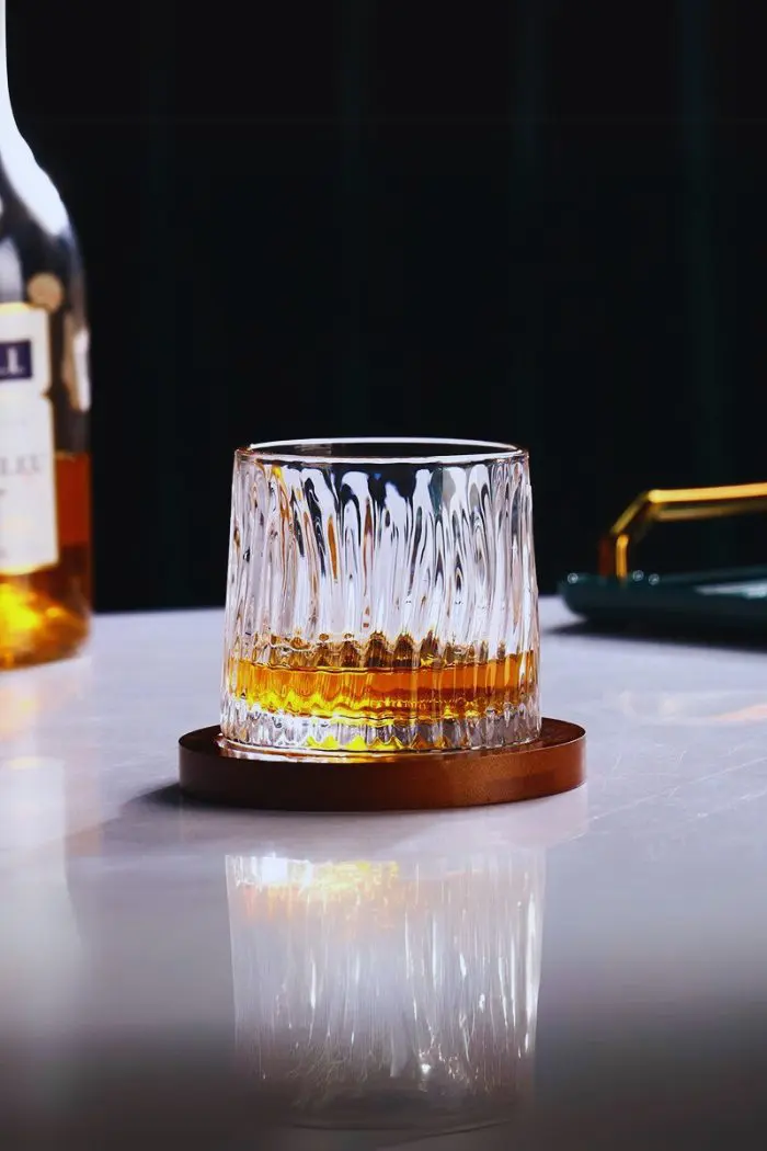 Verre à whisky tumbler rempli, posé sur son socle en bois sur une table claire.