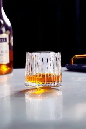 Verre à whisky tumbler texturé rempli, posé directement sur table claire sans sous-verre.