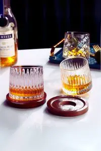 Deux verres à whisky tumbler remplis, l’un posé droit sur socle, l’autre incliné sur la table.