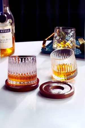 Deux verres à whisky tumbler remplis, l’un posé droit sur socle, l’autre incliné sur la table.