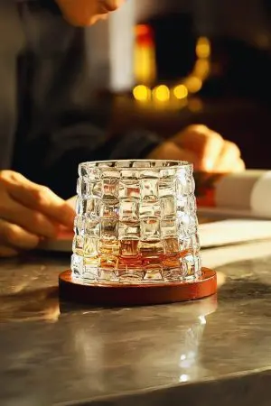 verre à whisky tumbler transparent posé sur un socle en bois sur une table brillante
