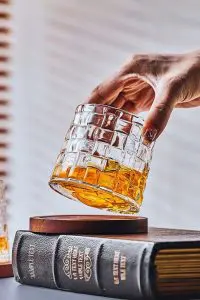 verre à whisky tumbler incliné tenu par une main au-dessus d’un socle en bois