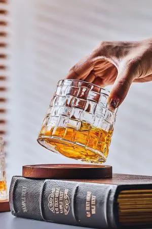 verre à whisky tumbler incliné tenu par une main au-dessus d’un socle en bois