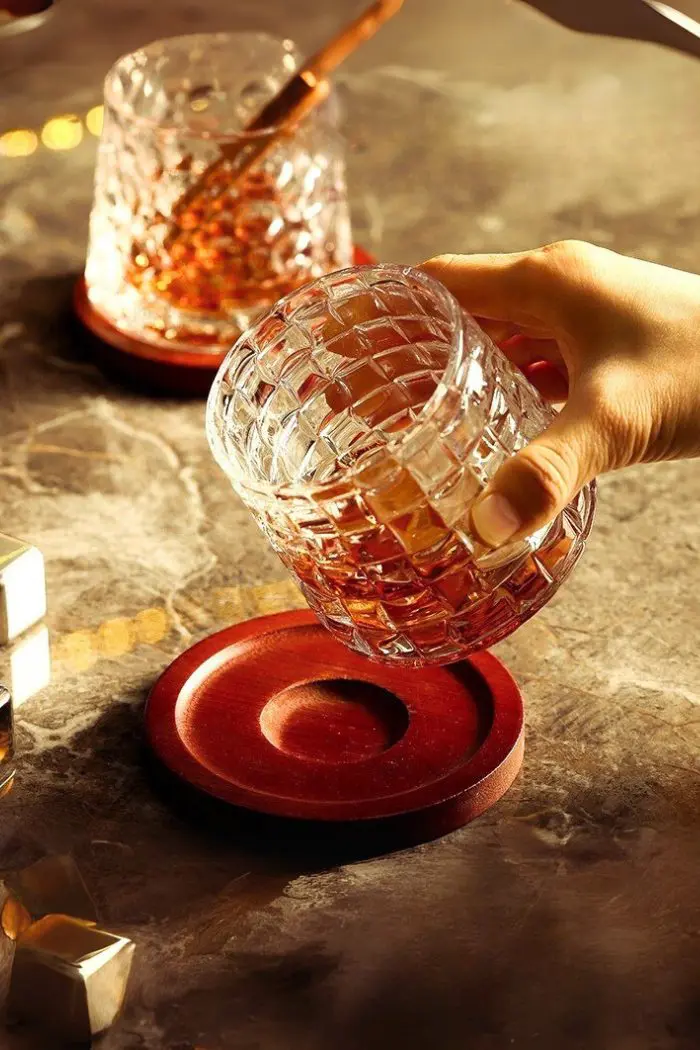 verre à whisky tumbler tenu par une main au-dessus d’un socle en bois