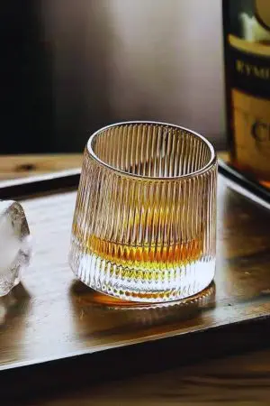 Verre à whisky tumbler vintage en verre nervuré posé sur un plateau en bois