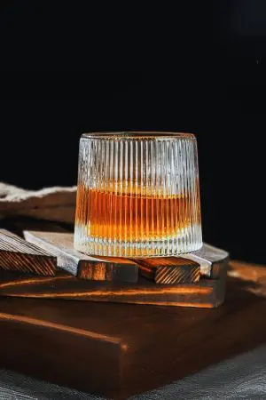 Verre à whisky tumbler nervuré incliné sur un plateau en bois clair
