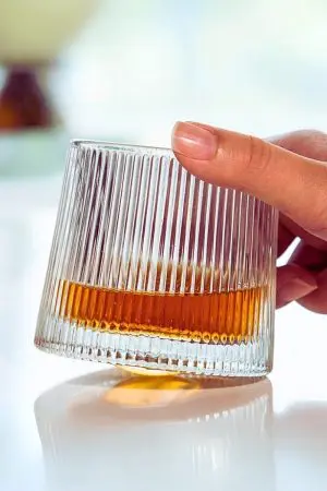 Verre à whisky tumbler nervuré incliné rempli de spiritueux foncé