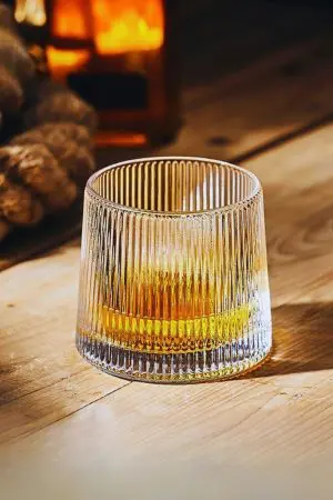Verre à whisky tumbler nervuré tenu en main sur fond blanc
