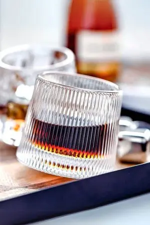 Verre à whisky tumbler nervuré incliné sur surface blanche réfléchissante