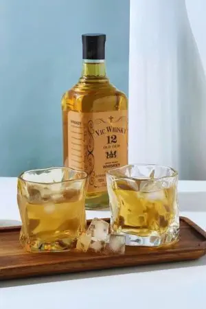 Verre à whisky en cristal teinté rempli de whisky et glaçons – Design ondulé et élégant.