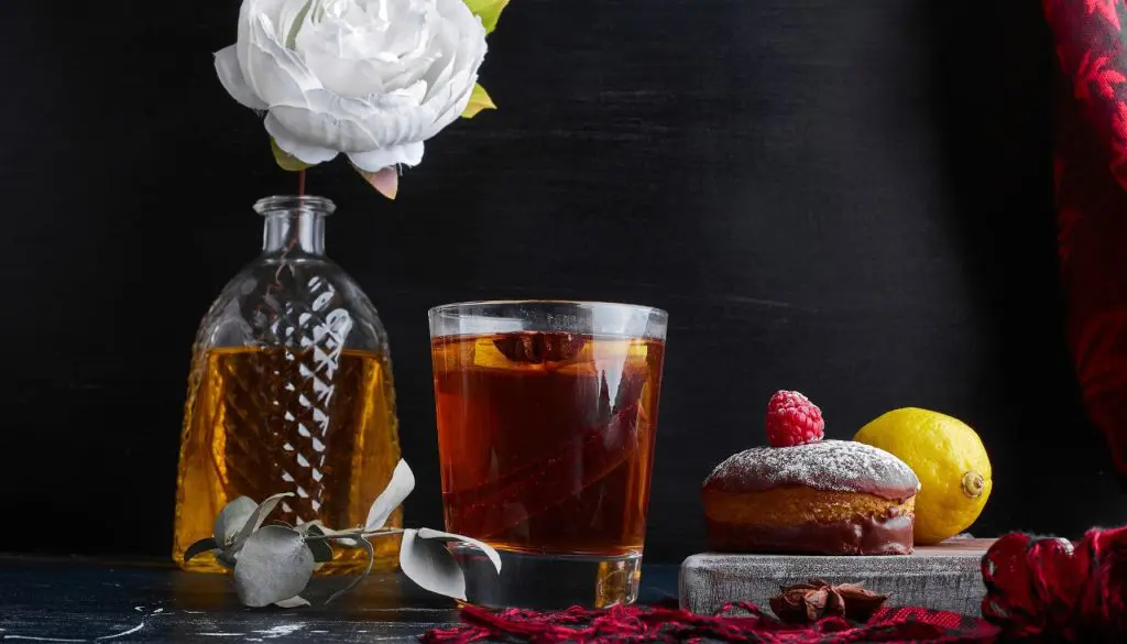 verre de whisky avec un petit gâteau au chocolat et citron, framboise et bouteille décorative, ambiance sombre