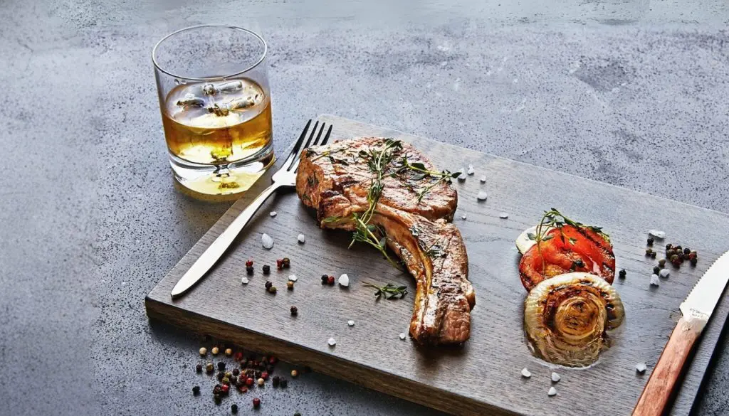 côte de viande grillée servie avec un verre de whisky sur une planche de bois
