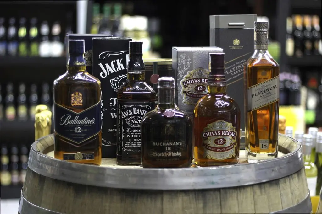 Assortiment de whiskies de marque exposés sur un tonneau en bois dans une cave ou un bar spécialisé.