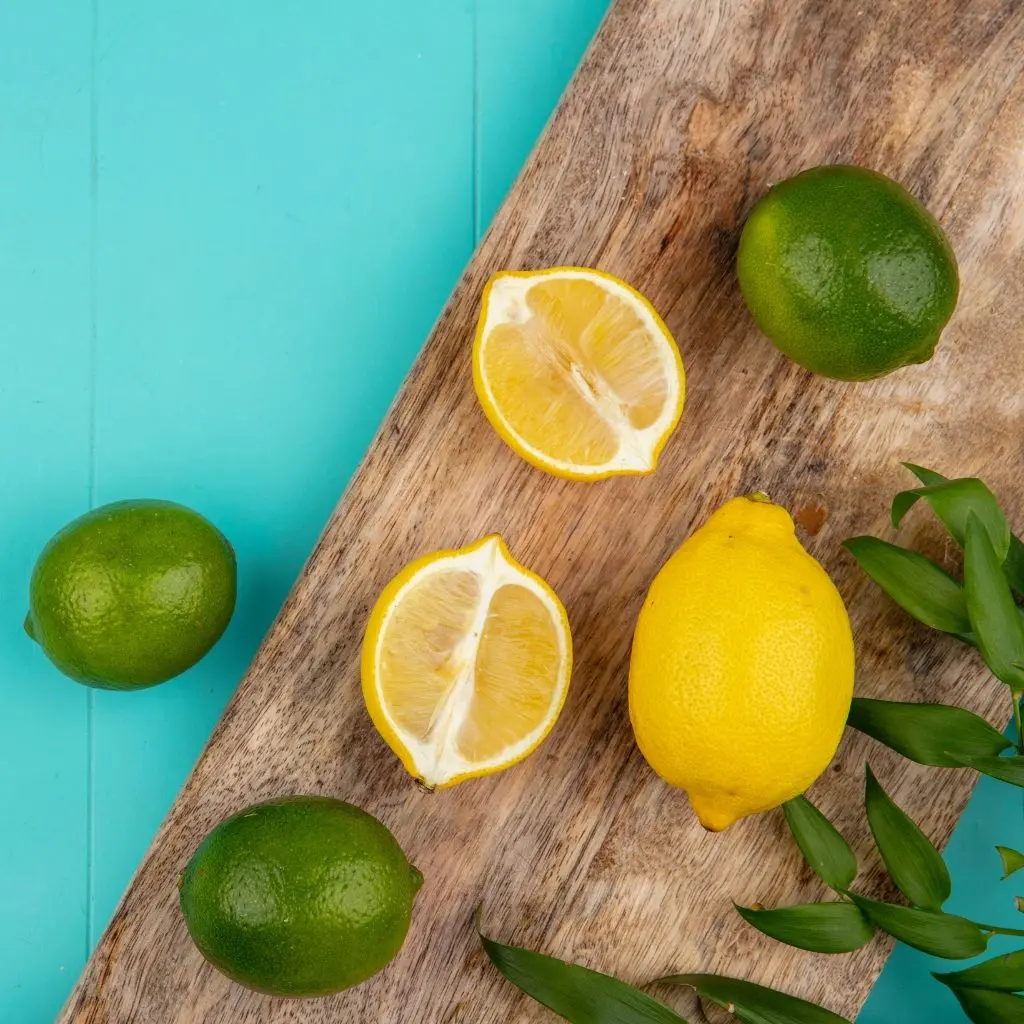 Citrons verts et citrons jaunes entiers et coupés posés sur une planche en bois