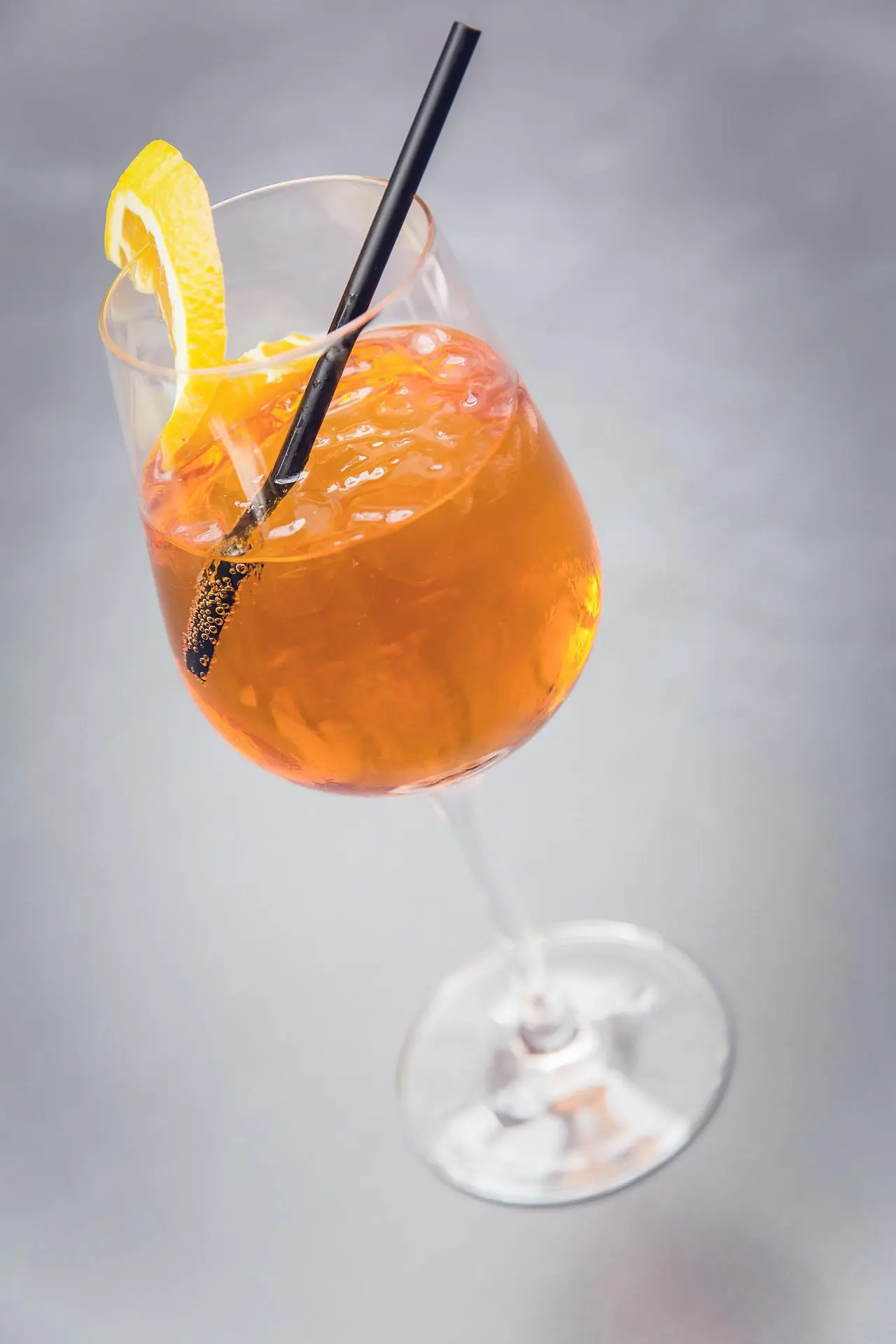 Verre à pied rempli d’un cocktail London Collins doré, avec glaçons, zeste de citron et paille noire