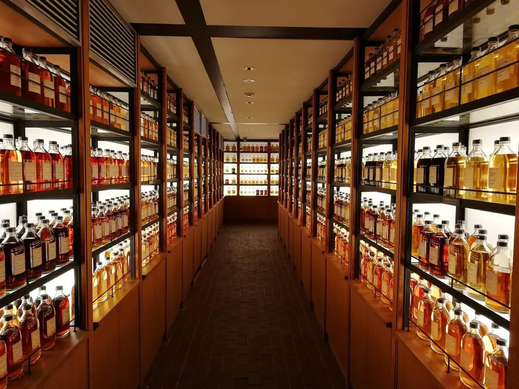 Longue allée bordée d’étagères remplies de bouteilles de whisky éclairées dans une cave ou une boutique spécialisée.