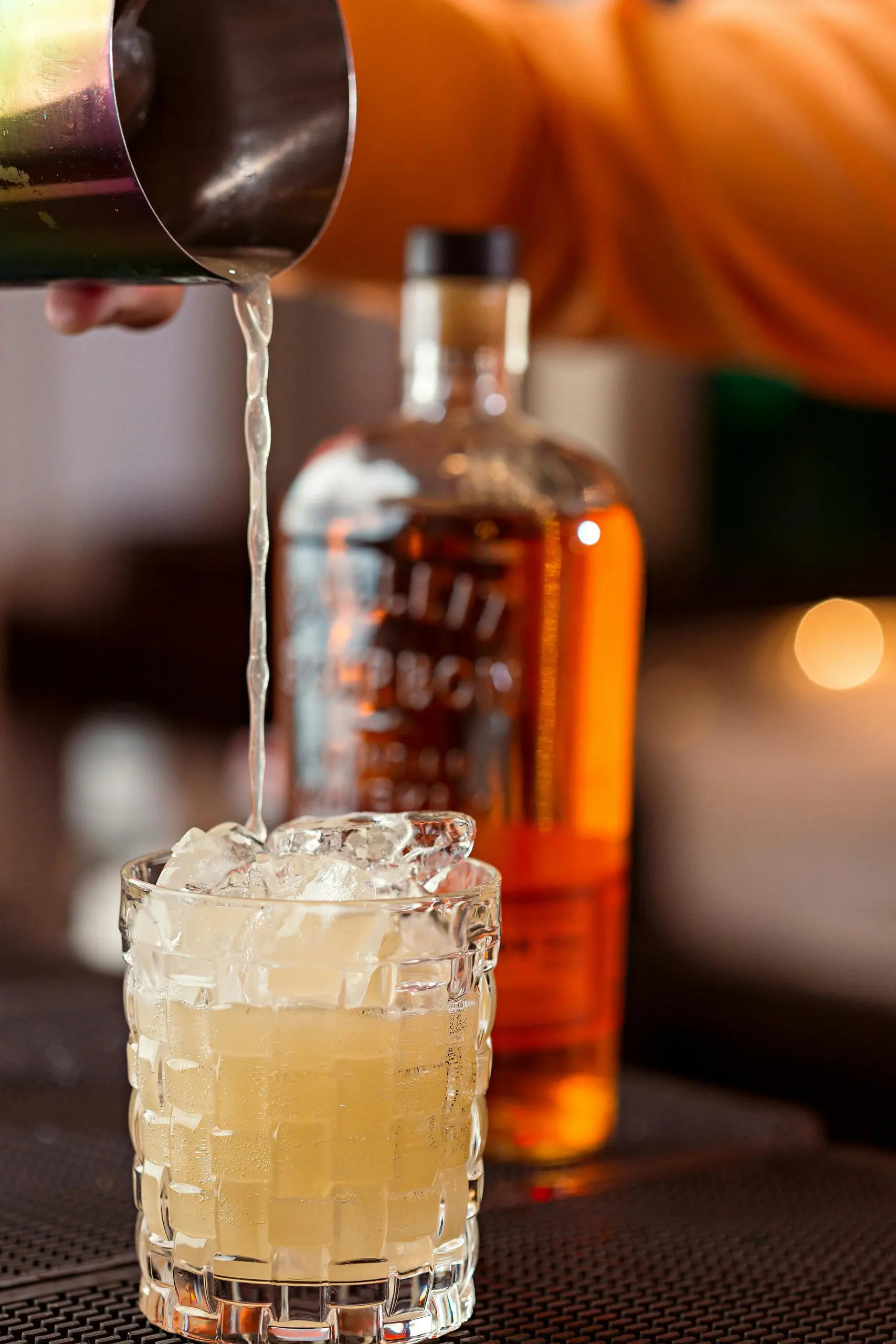 Préparation d’un Whisky Sour avec glaçons, shaker et bouteille de bourbon en arrière-plan