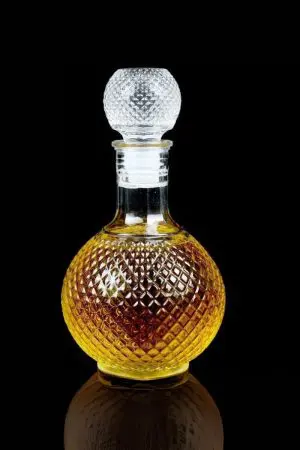 carafe à whisky ronde en verre 1 litre faceted sphere sur table en bois, bouteille sphérique à motifs facettés et bouchon assorti, lumière naturelle ambiance salon chic