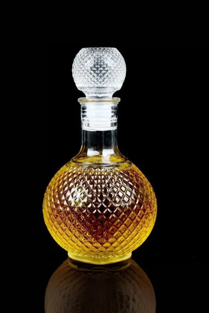 carafe à whisky ronde en verre 1 litre faceted sphere sur table en bois, bouteille sphérique à motifs facettés et bouchon assorti, lumière naturelle ambiance salon chic
