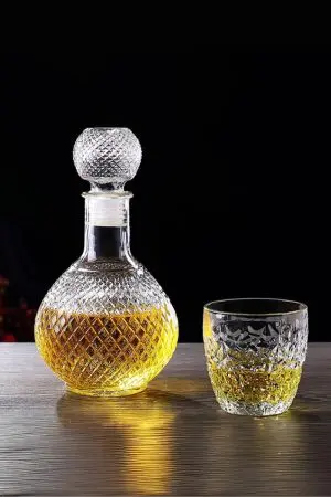 carafe à whisky ronde en verre faceted sphere posée sur plateau bois, accompagnée d’un verre à whisky rempli et glaçons, ambiance dégustation raffinée