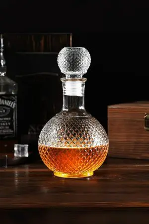 carafe à whisky ronde en verre faceted sphere vue de dessous, base sculptée, whisky doré visible à travers le verre taillé, lumière naturelle