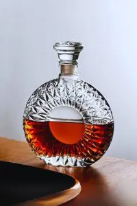 carafe à whisky ronde en verre taillé, posée sur une table en bois avec un liquide ambré