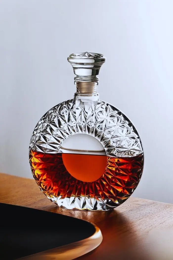 carafe à whisky ronde en verre taillé, posée sur une table en bois avec un liquide ambré