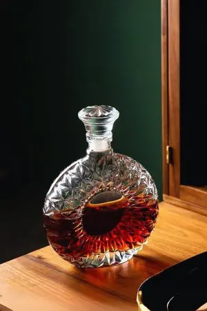 carafe à whisky en verre taillé ronde, remplie de whisky brun, posée sur une table en bois