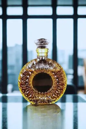 carafe à whisky ronde en verre gravé doré, posée sur une table en verre avec fond urbain flouté