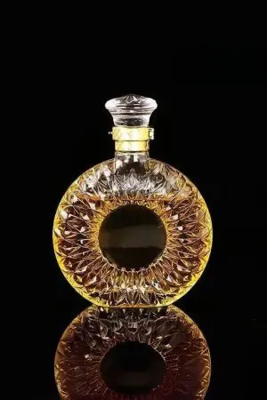 carafe à whisky en verre gravé posée sur une surface noire réfléchissante, remplie de whisky doré