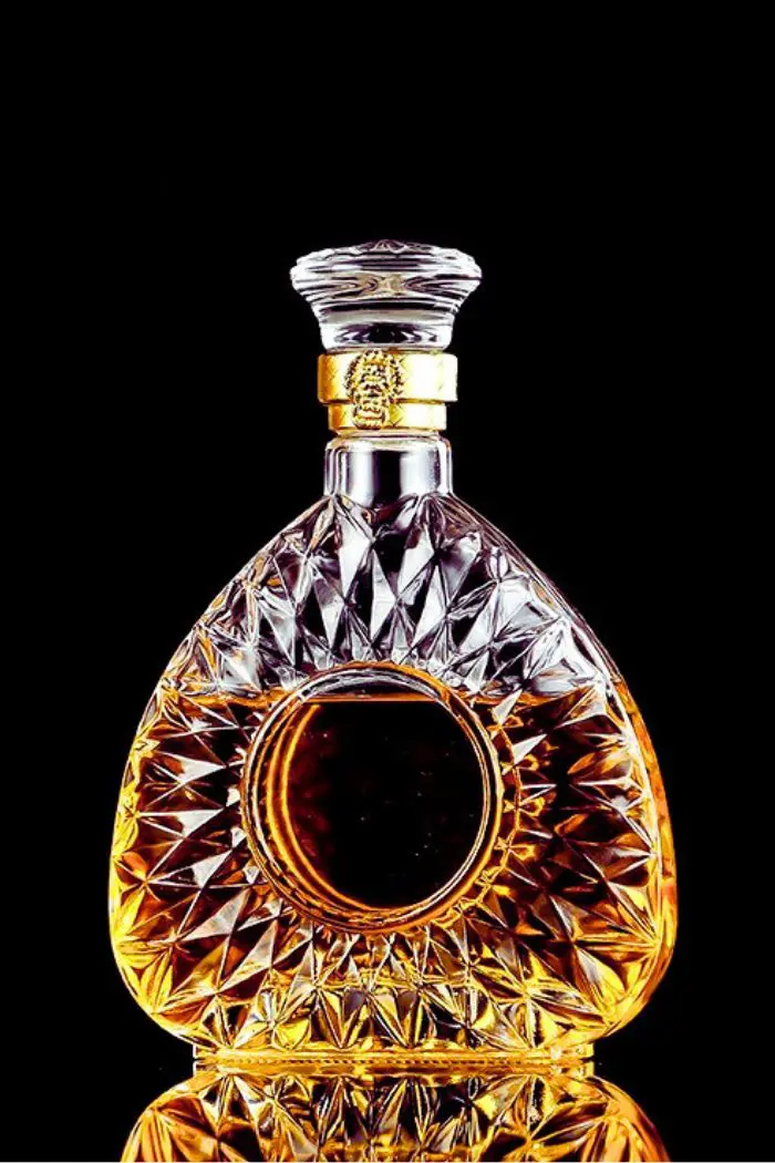 carafe à whisky ronde en verre taillé, remplie de whisky ambré, accompagnée d’un verre assorti, posées sur une table