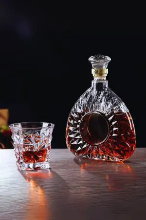 carafe à whisky ronde en verre taillé, remplie de whisky foncé, posée à côté d’un verre assorti sur une table