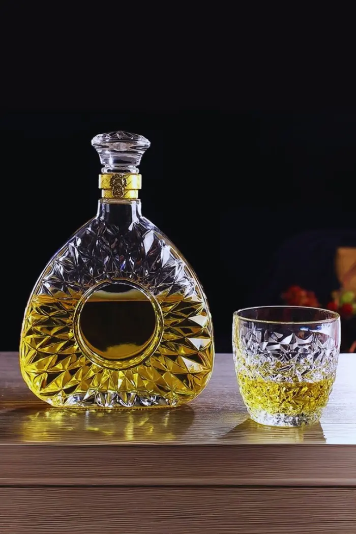 carafe à whisky ronde en verre taillé, bouchon avec bague dorée, remplie de whisky doré, posée seule sur une table