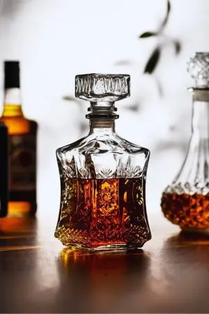 carafe à whisky en verre taillé, remplie de whisky ambré, posée sur une table en bois