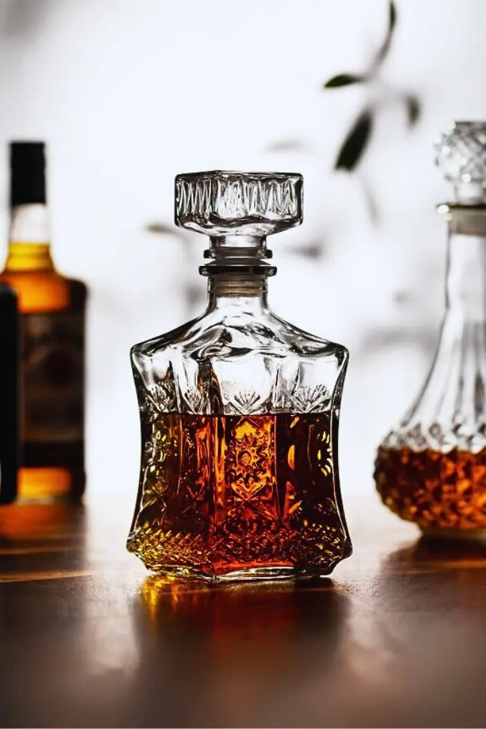 carafe à whisky en verre taillé, remplie de whisky ambré, posée sur une table en bois