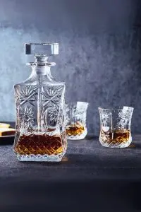 carafe à whisky en verre taillé, partiellement remplie, accompagnée de deux verres assortis sur fond gris