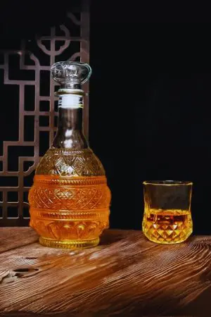carafe à whisky en verre gravé, remplie de liquide ambré, posée sur une table en bois
