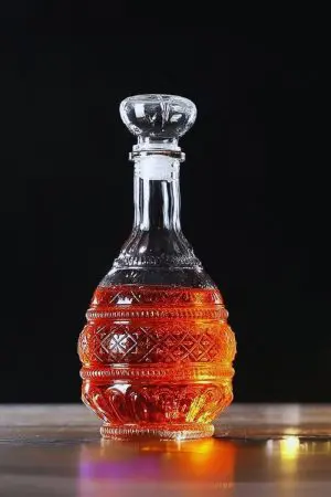 carafe à whisky bombée en verre gravé, remplie de whisky, posée sur table claire