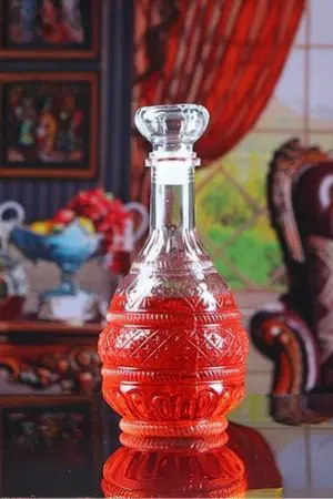 carafe à whisky gravée en verre, remplie, posée à côté d’un verre à pied sur table bois