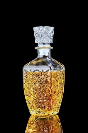 Carafe à whisky rétro en verre transparent gravé, remplie de whisky, posée sur fond noir.