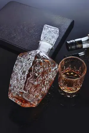 Carafe à whisky rétro en verre gravé, couchée avec son bouchon, à côté d’un verre rempli.