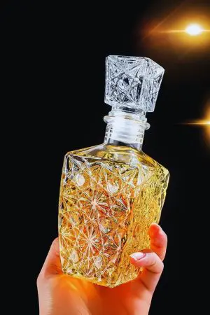 Carafe à whisky rétro en verre gravé tenue en main, fond noir avec éclairage jaune.