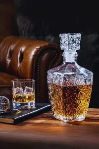 Carafe à whisky rétro gravée posée sur une table en bois à côté d’un verre rempli de glaçons.
