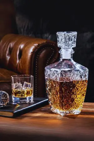 Carafe à whisky rétro gravée posée sur une table en bois à côté d’un verre rempli de glaçons.