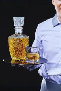 Carafe à whisky rétro en verre gravé posée sur un plateau avec un verre, serveur en chemise blanche.