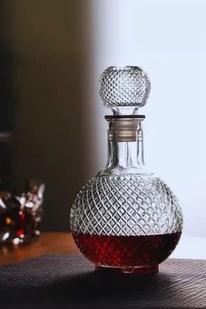 carafe à whisky boule en verre gravé, remplie de whisky ambré, posée sur une surface réfléchissante