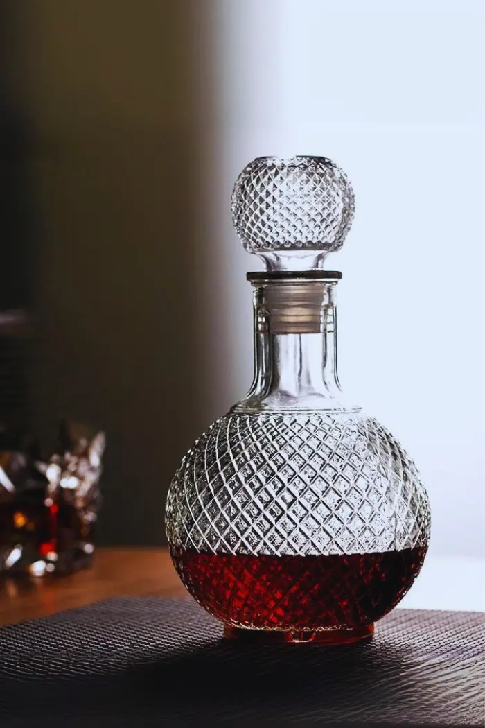 carafe à whisky boule en verre gravé, remplie de whisky ambré, posée sur une surface réfléchissante