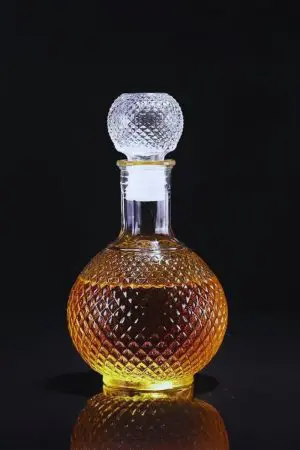 carafe à whisky boule gravée, posée sur un plateau rond, bouteille à l’arrière-plan flou