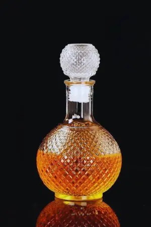 carafe boule à whisky en verre gravé, remplie de whisky ambré, posée sur fond noir